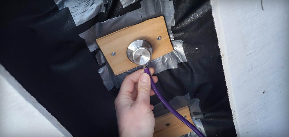 stethoscope being used to listen at the entrance of a bee hive